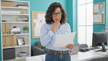 Orta yaşlı İspanyol iş kadını ofiste belge okuyor.