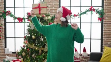 Beyaz saçlı, olgun İspanyol bir kadın Noel hediyesi tutuyor ve evde dans ediyor.