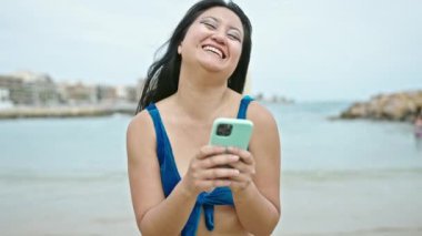 Genç Çinli turist plajda akıllı telefon kullanarak bikini giyiyor.