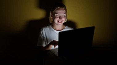 Sarışın genç kadın, sarı arka planda kutlama yaparken dizüstü bilgisayar kullanıyor.