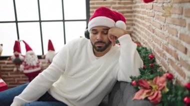 Afro-Amerikalı adam evinde Noel şapkası takarak kanepede uyuyor.