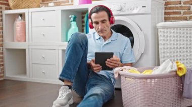 Çamaşır odasında çamaşır makinesi bekleyen orta yaşlı bir adam müzik dinliyor.