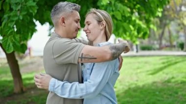 Kadın ve erkek parkta öpüşürken birbirlerine sarılıyorlar.