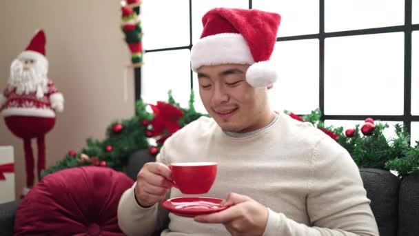 Ung Kinesisk Man Dricker Kaffe Sitter Soffan Jul Dekoration Hemma — Stockvideo