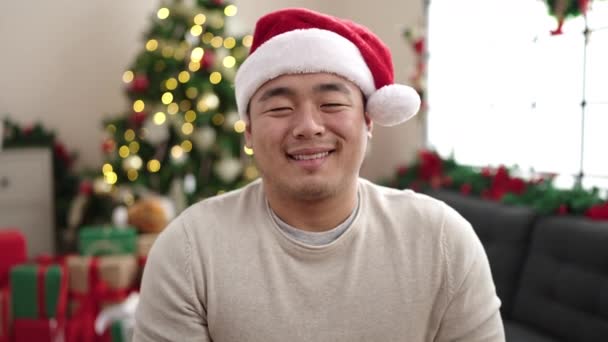 自宅でクリスマスツリーでソファーに座って自信を持って微笑む若い中国人男性 — ストック動画