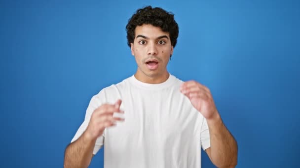 孤立したブルーの背景に驚きの表情で立っている若いラテン人男性 — ストック動画