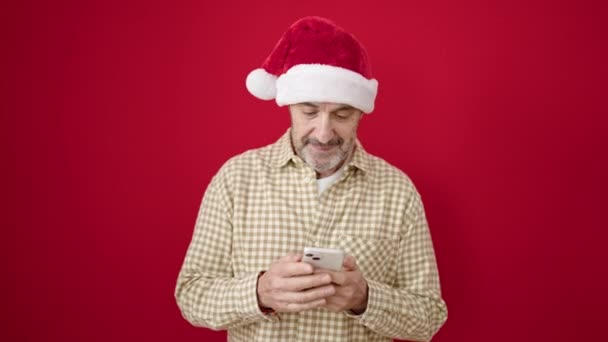 Mann Mittleren Alters Trägt Weihnachtsmütze Mit Smartphone Vor Isoliertem Roten — Stockvideo
