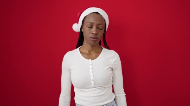 クリスマスの帽子をかぶったアフリカ系アメリカ人女性は 孤立した赤い背景の上にストレスを受けた表現で立っています — ストック動画