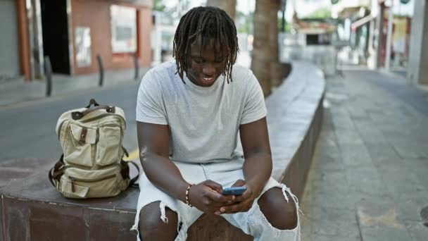 Hombre Afroamericano Usando Teléfono Inteligente Sentado Banco Celebrando Calle — Vídeo de stock