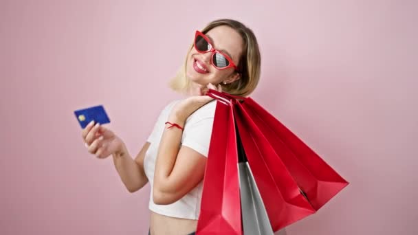 単離されたピンクの背景上のショッピングバッグとクレジットカードを保持している若い金髪の女性の顧客 — ストック動画