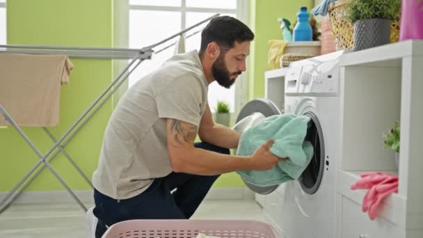 洗濯室で笑顔で親指で服を洗っている若いヒスパニック男性 — ストック動画