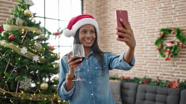 アフリカ系アメリカ人女性が自宅でクリスマスを祝うスマートフォンでワインを飲むことでセルフィーを作ります — ストック動画