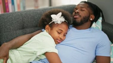 Afrikalı Amerikalı baba ve kız kanepede yatıp evde uyuyorlar.