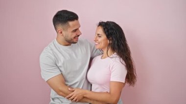 Erkek ve kadın çift gülümsüyor, kendilerine güveniyorlar, pembe arka planda sarılıyorlar.