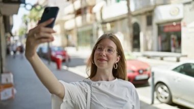 Young blonde woman smiling confident making selfie by the smartphone at street