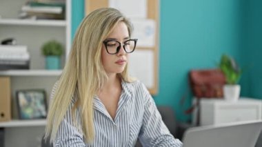 Genç sarışın iş kadını ofiste çalışırken laptop kullanıyor.