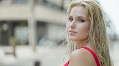 Ciddi bir ifadeyle ayakta duran genç sarışın kadın kendini geri çeviriyor ve sokakta yürüyor.