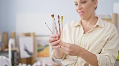 Resim stüdyosunda fırçalara bakan genç sarışın sanatçı.