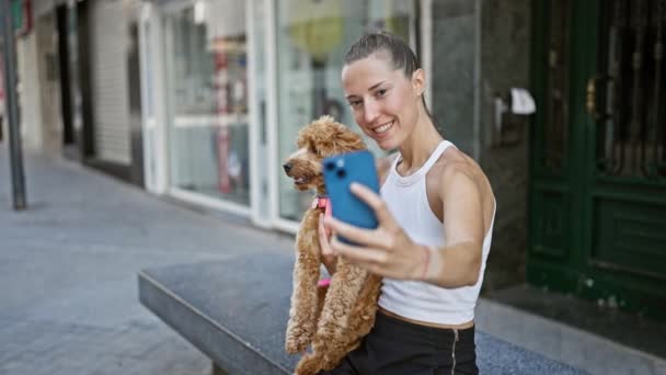 ストリートでベンチに座っているスマートフォンでセルフィー写真を撮る犬を持つ若い白人女性 — ストック動画