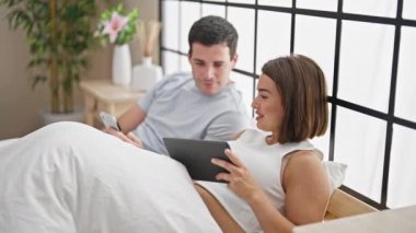 Akıllı telefon ve dokunmatik ped kullanan güzel bir çift yatak odasında oturuyor.