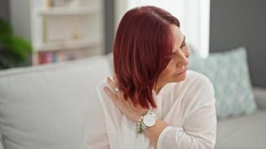 Orta yaşlı bir kadın koltuğunda oturmuş evinde omuz ağrısı çekiyor.