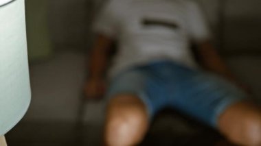 Kanepede oturan İspanyol genç adam evde uzaktan kumandayla yatıyor.