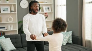 Afrikalı Amerikalı baba ve kız gülümseyerek evde dans ediyorlar.
