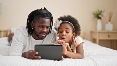 Afrikalı Amerikalı baba ve kızı yatak odasında dokunmatik yastıkta uzanmış videolar izliyorlar.