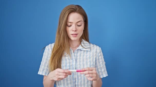 年轻的金发女子带着自信的笑容 在孤寂的蓝色背景下举行怀孕测试 — 图库视频影像