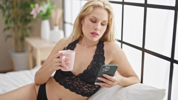 Ung Blond Kvinna Bär Underkläder Med Smartphone Dricka Kaffe Sovrummet — Stockvideo