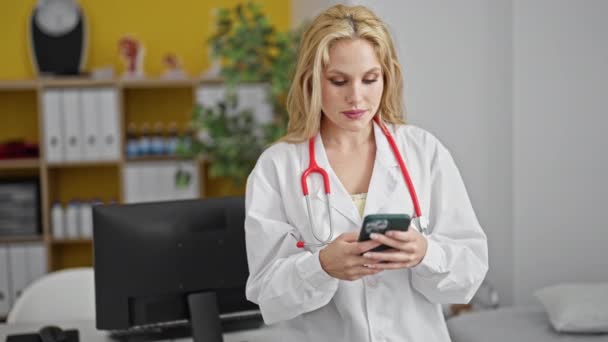 年轻的金发女医生在诊所用智能手机微笑 — 图库视频影像