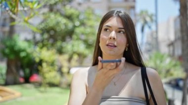 Genç, güzel İspanyol kadın parkta akıllı telefonuyla sesli mesaj yolluyor.