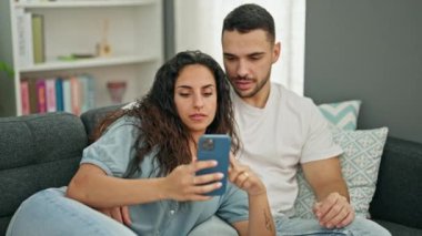 Erkek ve kadın akıllı telefon kullanıyor. Kanepede oturmuş evde kutlama yapıyorlar.