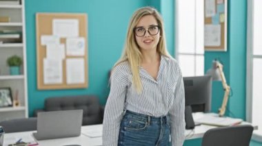 Genç sarışın iş kadını. Ofiste kameraya işaret eden bir jest yapıyor.