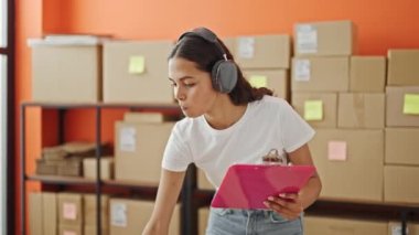Afrikalı Amerikalı kadın ecommerce iş işçisi. Belgeye yazı yazıyor. Ofiste müzik dinliyor.