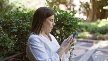 Parkta akıllı telefon kullanarak sırıtan genç ve güzel bir İspanyol kadın.