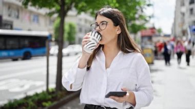 Akıllı telefon kullanan genç, güzel İspanyol kadın Madrid sokaklarında kahve içiyor.