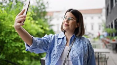 Genç ve güzel İspanyol kadın açık hava kafeteryasında akıllı telefonuyla selfie çekiyor.