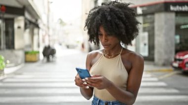 Sokakta gülümseyen akıllı telefon kullanan Afrikalı Amerikalı kadın.