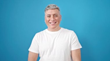 İzole edilmiş mavi arka planda gülümseyen beyaz bir genç.