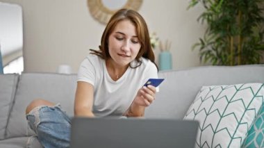 Laptop ve kredi kartıyla alışveriş yapan genç bir kadın evdeki koltukta oturmuş kutlama yapıyor.