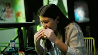 Genç ve güzel İspanyol kadın restoranda lezzetli hamburgerler yiyor.