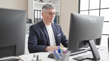 Kafkasyalı genç bir iş adamı bilgisayar kullanıyor. Ofiste kollarını açarken gözlük takıyor.