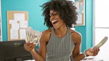 Afrikalı Amerikalı kadın iş kadını elinde dolarlarla ofiste gülümsüyor.
