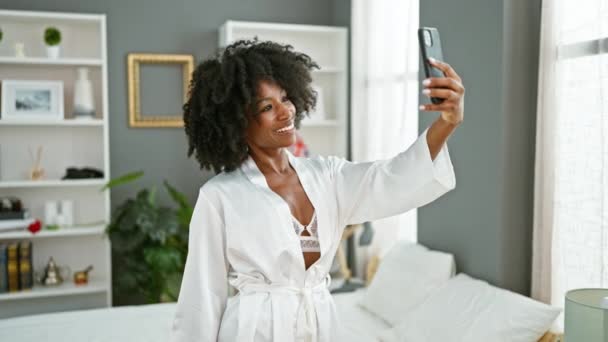 セクシーに見えるアフリカ系アメリカ人女性は寝室でスマートフォンでセルフィーを作ります — ストック動画