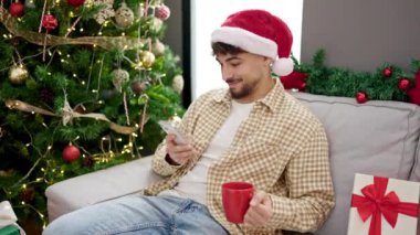 Noel Baba şapkalı yakışıklı genç adam ve Noel 'de oturma odasında akıllı telefon kullanıyor.