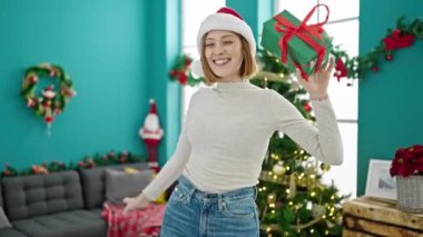 Genç sarışın kadın gülümsüyor kendinden emin bir şekilde evde Noel hediyesi alıyor.