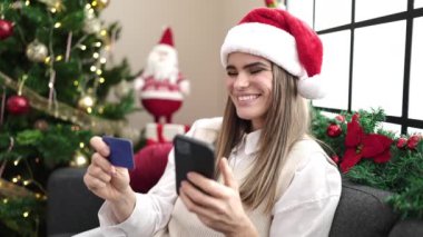 Güzel genç bir kadın Noel 'i akıllı telefon kullanarak ve kredi kartıyla online ödeme yaparak kutluyor. 