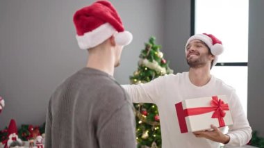 Mutlu genç baba ve oğul Noel Baba şapkalarını takmış hediyelerini tutuyor ve gülümsüyor.