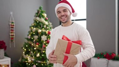 Noel Baba şapkalı, elinde hediye kutusuyla mutlu genç bir adam.